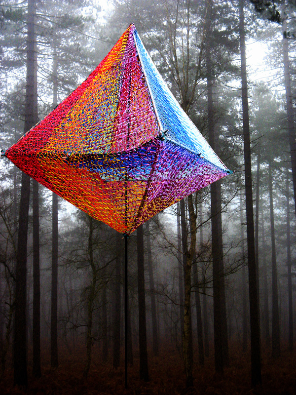 Art installation by Edith Meusnier. Multicoloured net sculpture in the form of a 3D diamond hanging in a misty forest.