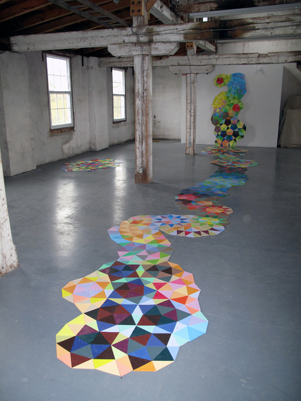 Piece by Piece, 2010 – an installation of three different triangular shapes created for the loft space at the Visual Arts Centre in Bowmanville Ontario. The masonite shapes, painted in 49 colours are a riff on pentagonal non-periodic tilings discovered by Roger Penrose. His original diamond shapes have been divided into triangles to allow for more colour variation. The installation was 42 feet long and between 3 and 6 feet wide.