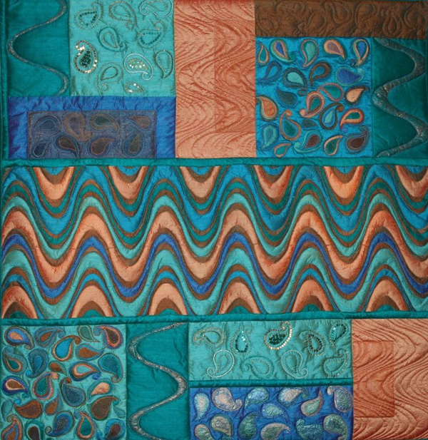 India (102 x 104 cm), Materials: silks, beads, angelwire

My husband made a business trip to India and brought along 6 large silk fabrics. The colours were difficult to combine, but according to my husband they are typical colours of India. Therefore, I wanted to create a real India-quilt with Indian motifs like the paisley patterns which are often used on scarves. I have used the motifs in different ways, with silk, angel wire, beads and sequins and simple quilting. To avoid the quilt becoming too busy, I also added some blocks with waves in it.
