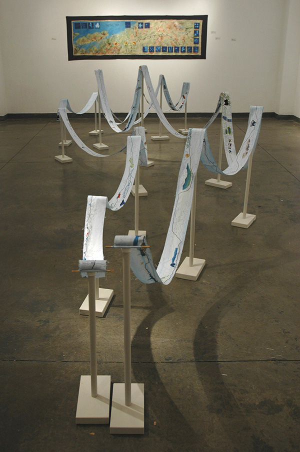 The Bike Trip Map 1998 (finished 2006), 240cm w x 60cm h, fabric paint, fabric printing, photo transfers, hand embroidery., AND The Bike Trip Spool 1998-ongoing, 10cm w x 2300cm long, dyed fabric, ink drawing, hand embroidery, wood and plastic stands