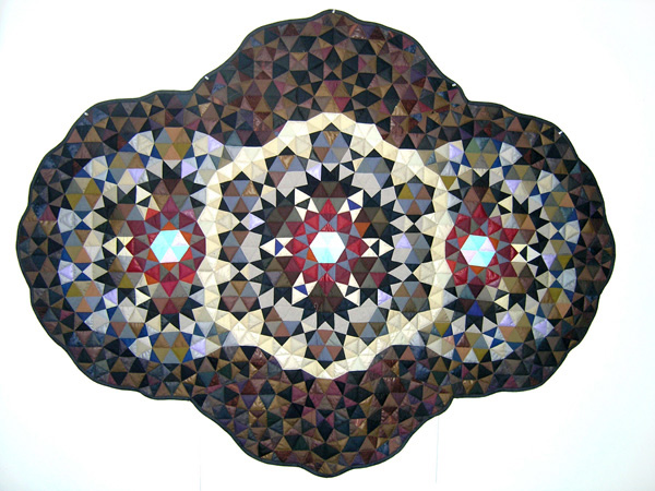 Cyclops, 2005, 84"x 65", textile hanging/quilt, machine pieced, hand quilted. The design derives from only two shapes, one equilateral triangle and a square with the same dimensions, divided into two or four smaller triangles. The geometric patterns generated using these shapes are infinitely variable. Colour, both hue and light/dark contrasts can cause particular shapes or groups of shapes to dominate or recede. The free form edge follows the shape of the geometric structure. Photo: Judith Tinkl.
