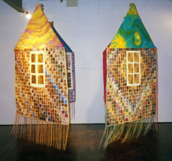 The House With the Golden Windows. Installation of four panels, each 6 feet high, 4 feet wide, double sided 1993. The outside walls are made from glossy magazine papers stitched to artist canvas, and hand stitched metallic fabric windows. Each of the four panels has a different roof colour, representing the four seasons, the four directions, the four times of day and the four ages of a woman. The inside of the walls are made from pieced and embroidered silk or cotton and have 'windows' made from stitched photographs of the views from inside the artist's Kenora house. This image is from the group exhibition Quilted Stories in A Space Gallery, Toronto , 1994. photo Judy Martin