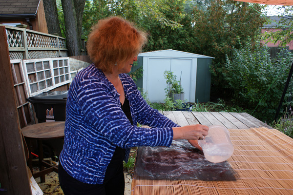 Sheila in her garden, wetting down the finished design in preparation for felting