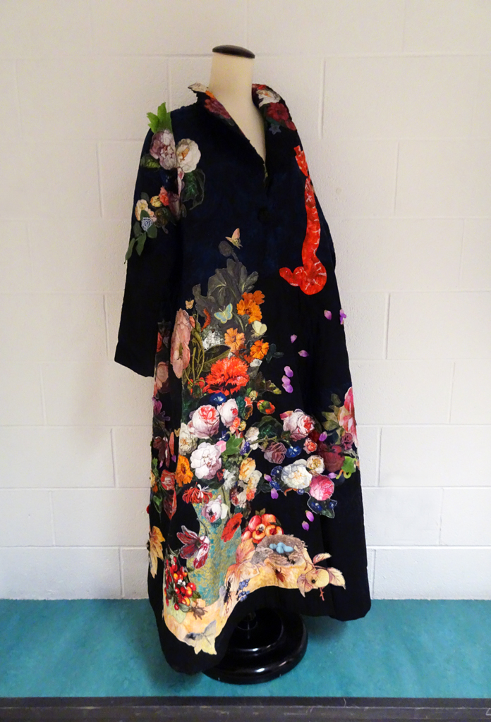 Marijke van Welzen: Still Life, 2017, 150H x 100W x 100D cm,  coat.
Materials: cotton, lining polyester, plastic insects, polyester leaves, fabric paint. Techniques: Textile collage, applique, thread painting, free motion machine stitching, fabric painting.