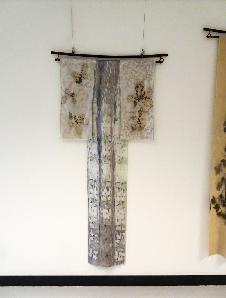 CLinda Kollofski: Clematis Logwood, 2017, 67H x 29W x .5D inches, woven silk charmeuse and cotton, flowers/ leaves, natural logwood dye. Technique: Ecoprinted with plants from my garden using their natural dyes and arashi shibori. Hung on bamboo hanger: 35W x 3H.