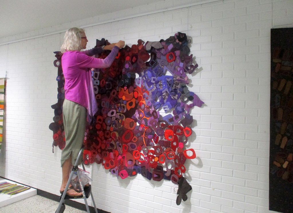 Festival installer Caren, installing work in the Covid Forever exhibition, World of Threads Festival 2023-24.