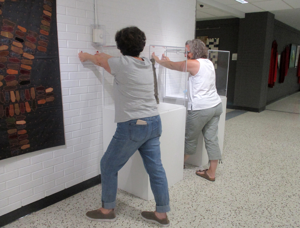 Festival installers, Carol and Heidi, installing work in the Covid Forever exhibition, World of Threads Festival 2023-24.