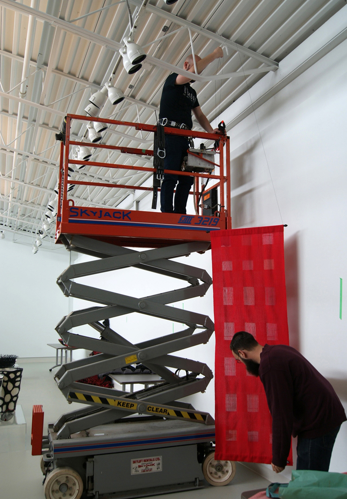 Festival Curator: Gareth and helper, installing artwork for The Red and the Black exhibition, World of Threads Festival 2014.